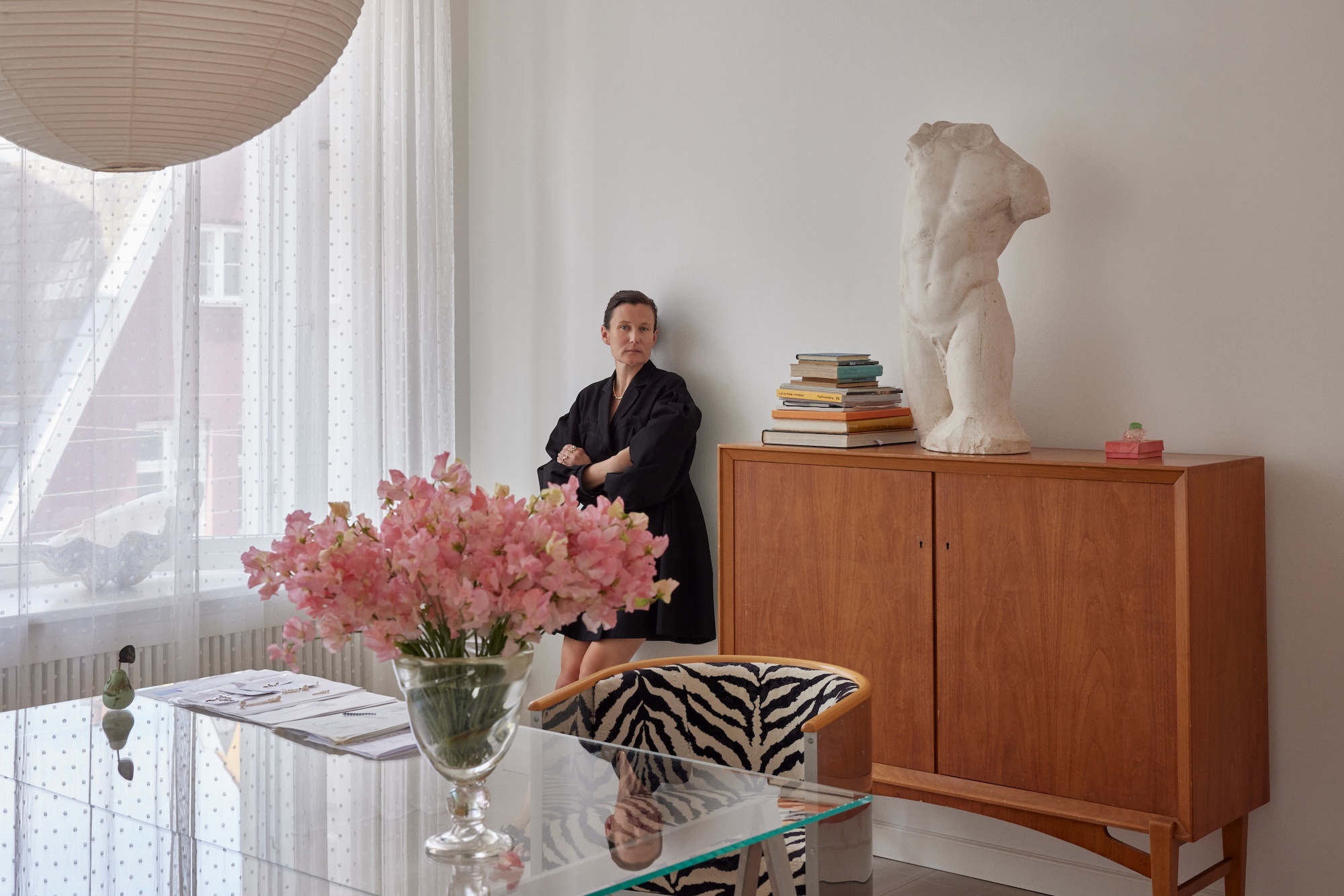 Sophie Bille Brahe in her New York showroom, standing beside a wooden cabinet topped with a plaster torso and stacked books
