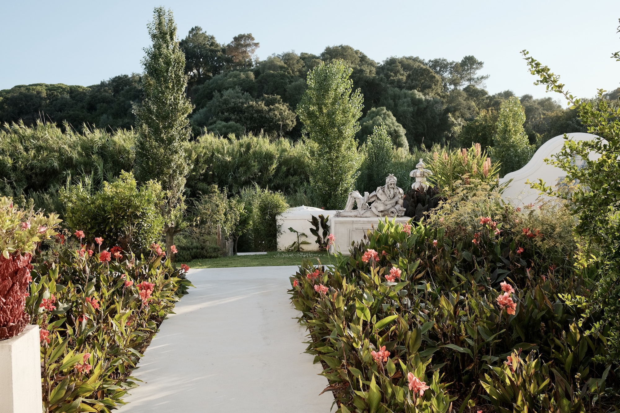 Garden path lined with red flowers leading to a white statue at Vermelho