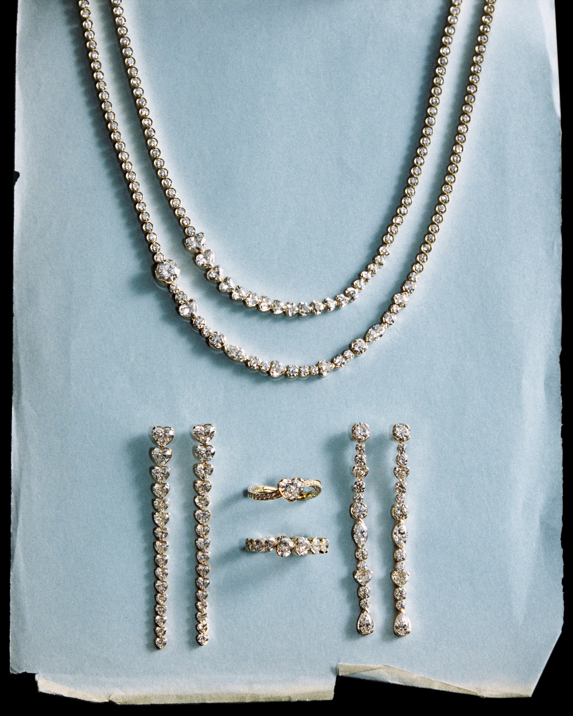 Diamond necklaces, earrings and rings laid out on pale blue paper