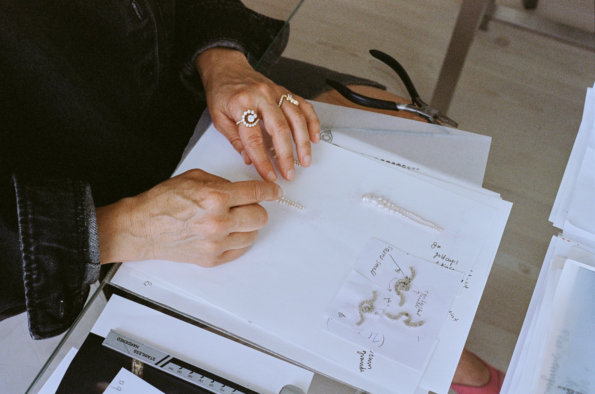 Hands arranging freshwater pearls and hand-drawn sketches on a workbench