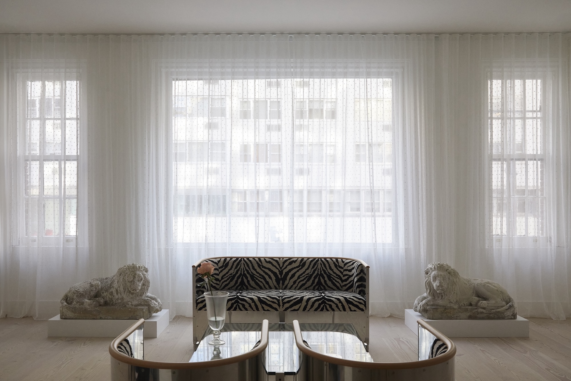 Stone lion statues flanking a zebra-striped sofa in front of sheer curtained windows