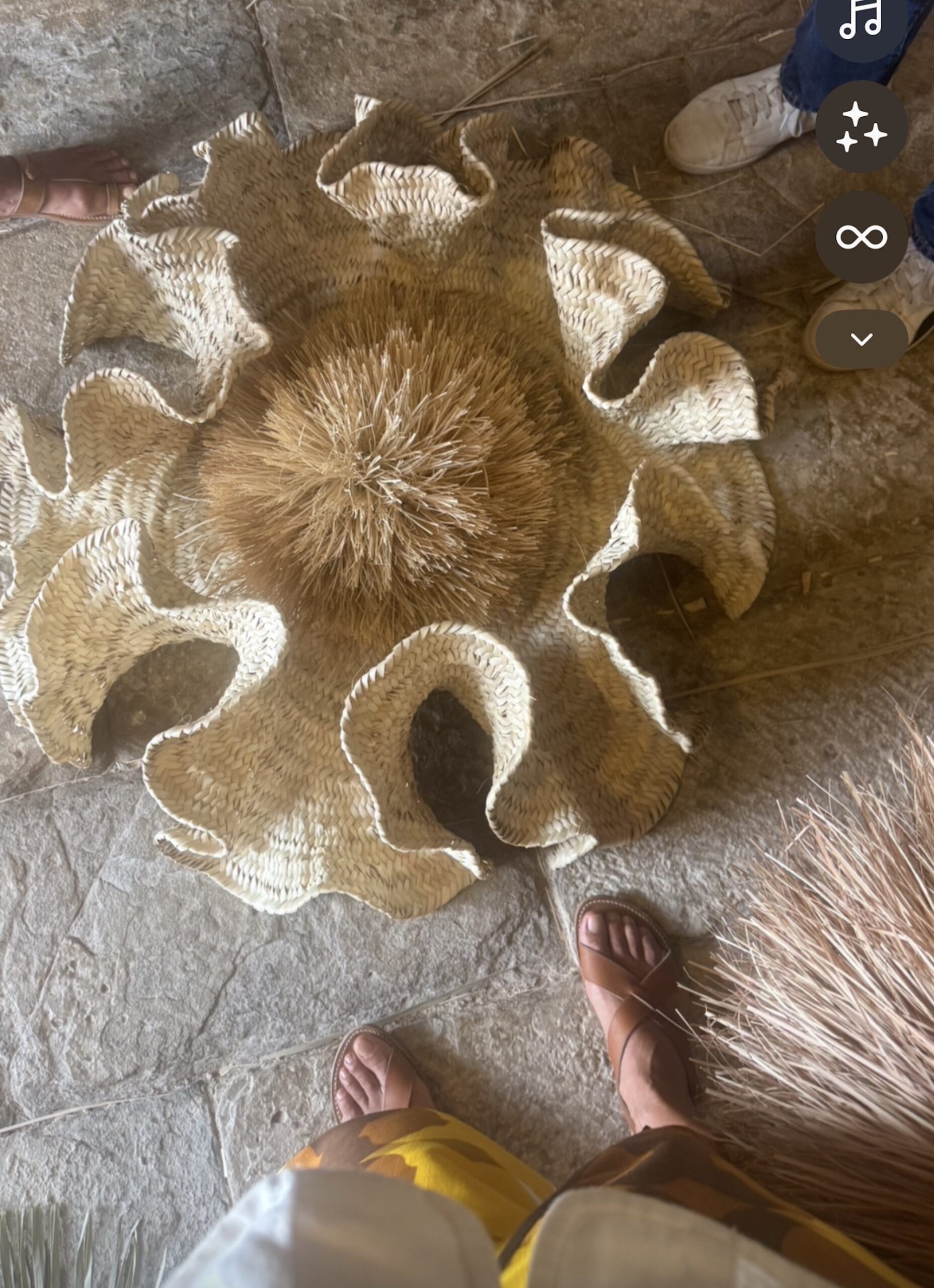A finished woven palm piece laid flat, showing its fringed centre and scalloped petals