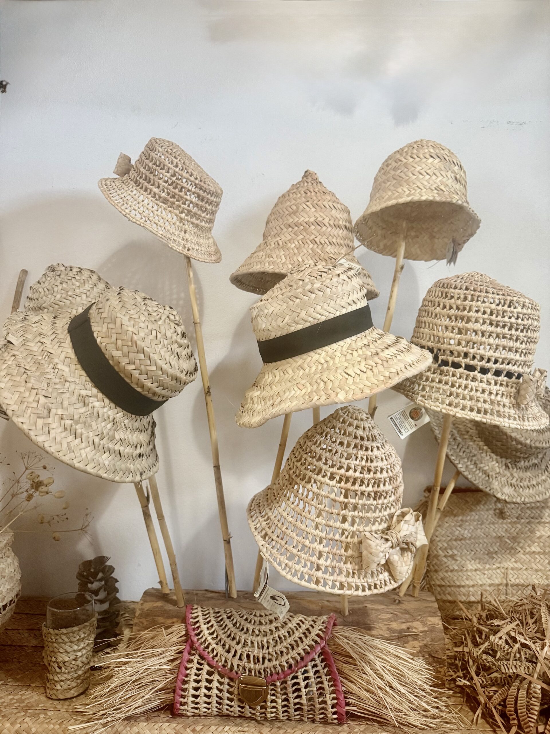 A row of finished straw hats alongside a woven clutch with leather trim