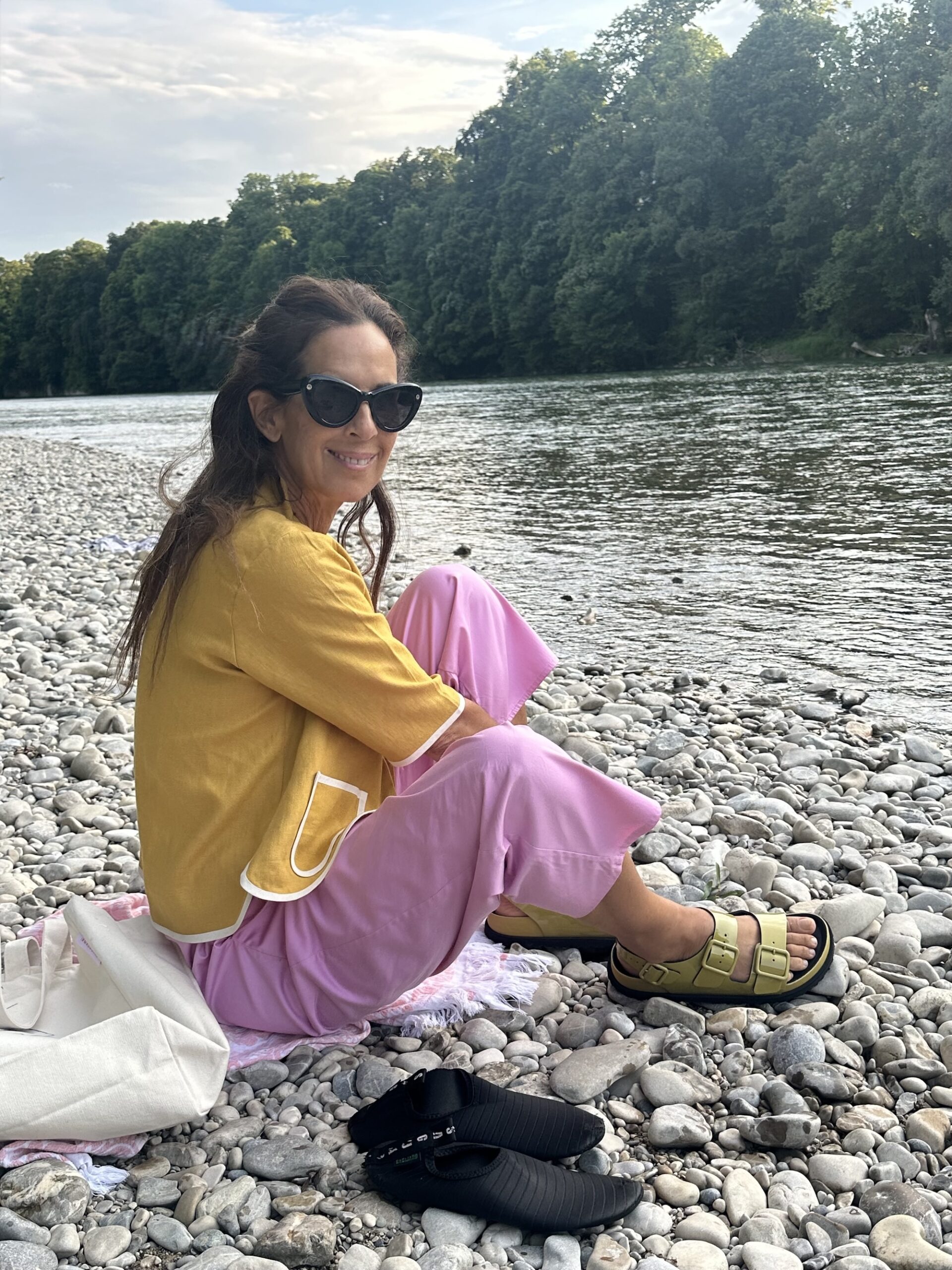 Woman sitting barefoot on river stones beside the water