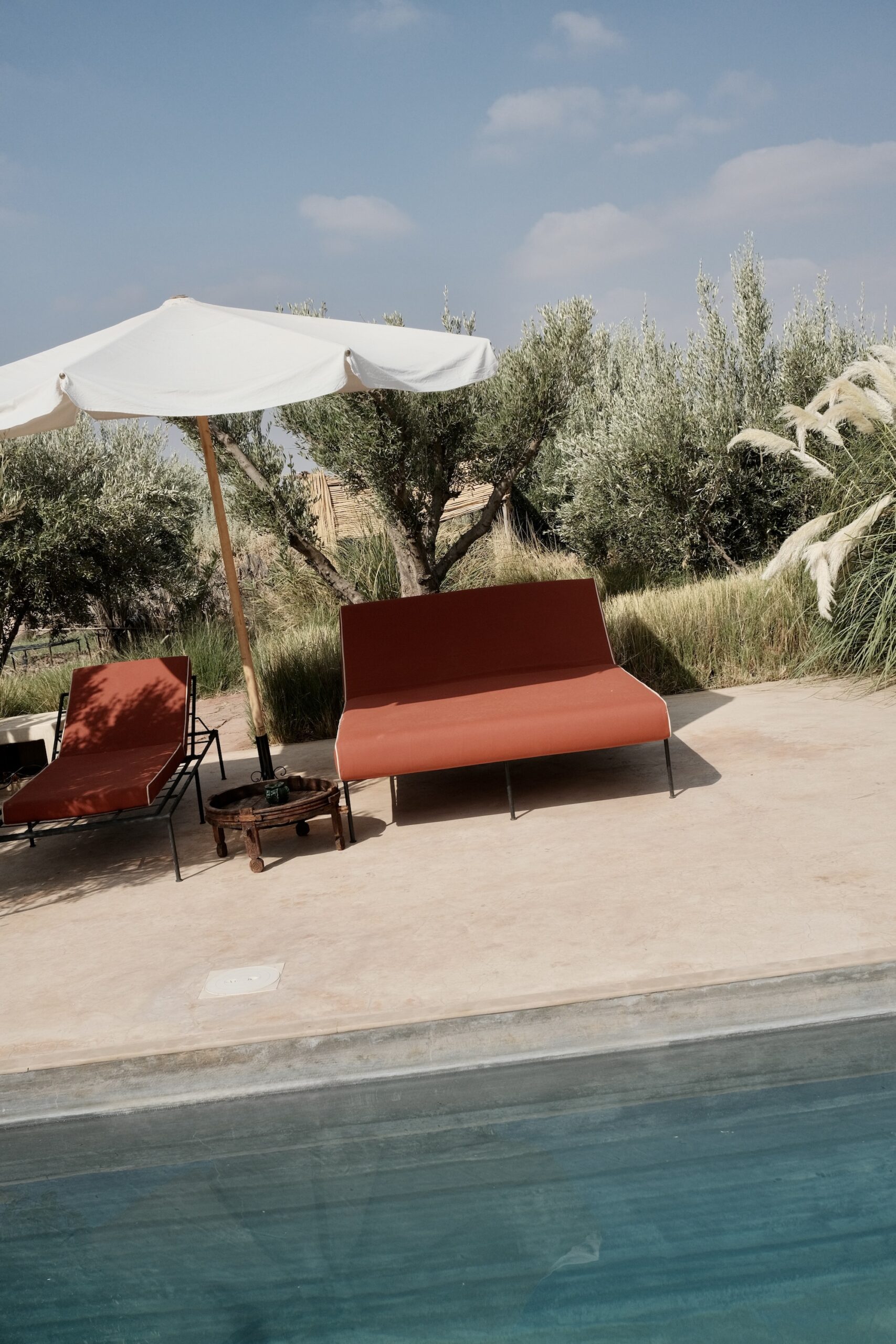 Terracotta poolside sofa and lounger under a white umbrella at Farasha Farmhouse