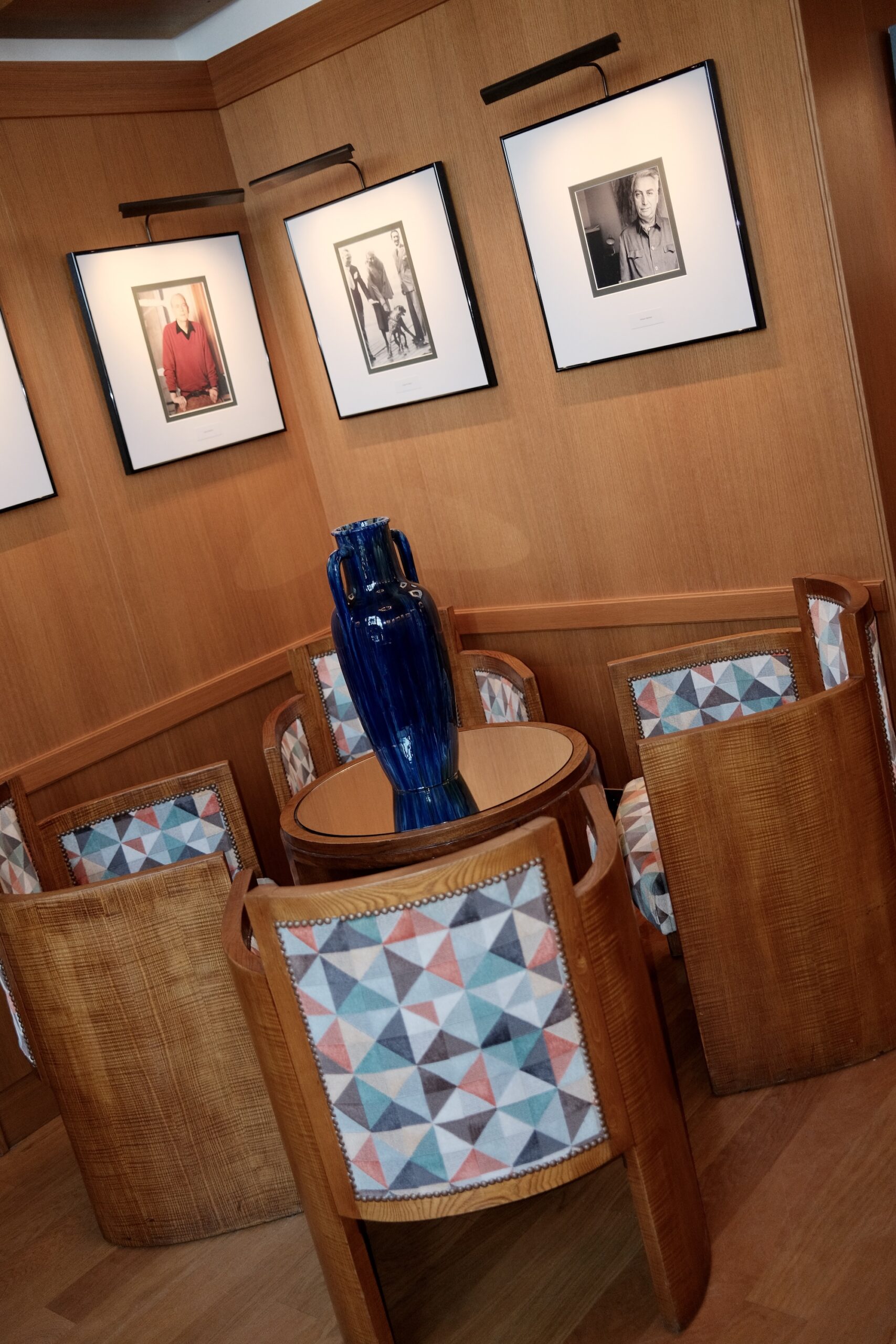 Portrait photographs above Art Deco armchairs and a blue vase in a salon at Hotel Belles Rives