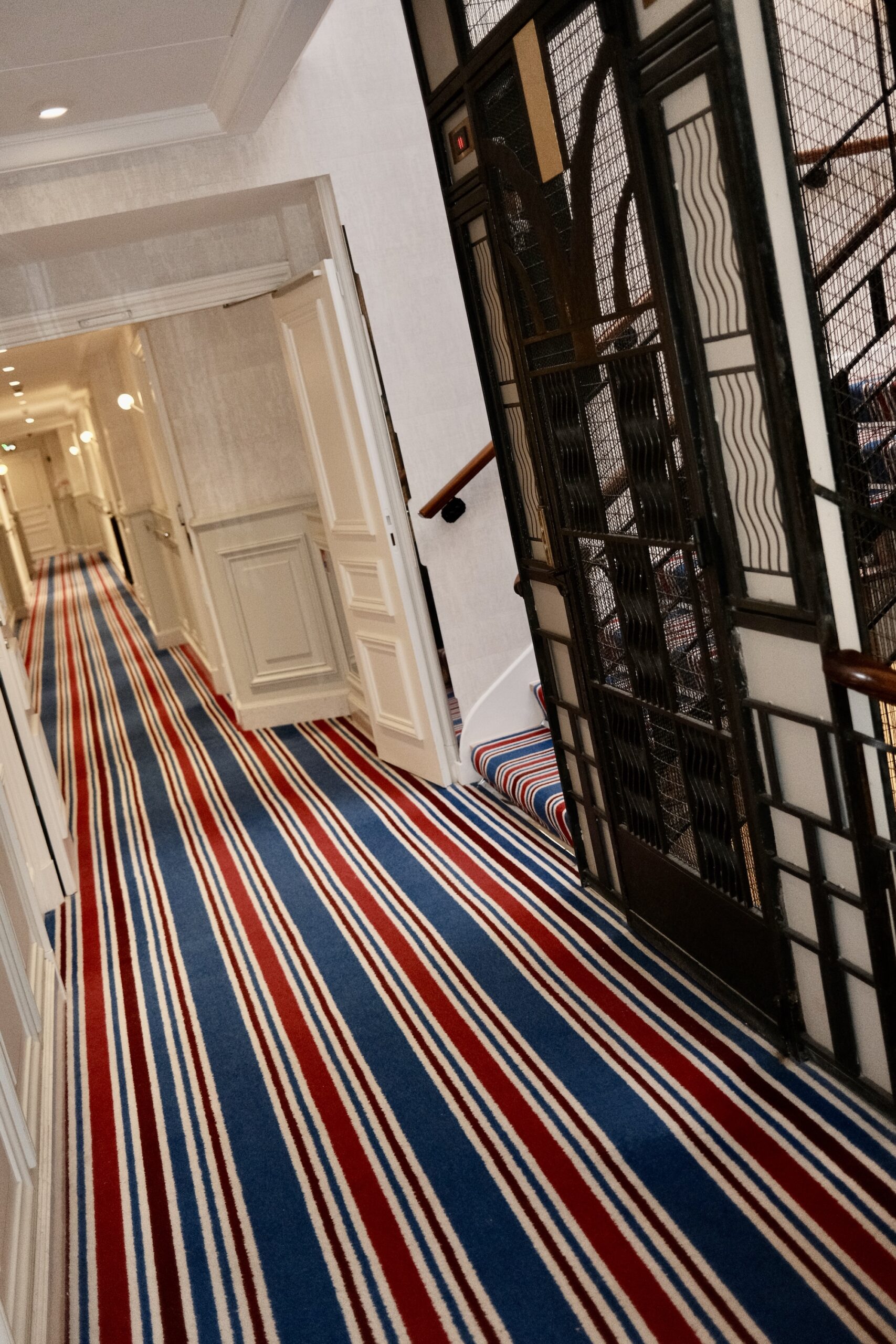 Striped red, white and blue carpet beside the original wrought iron lift at Hotel Belles Rives