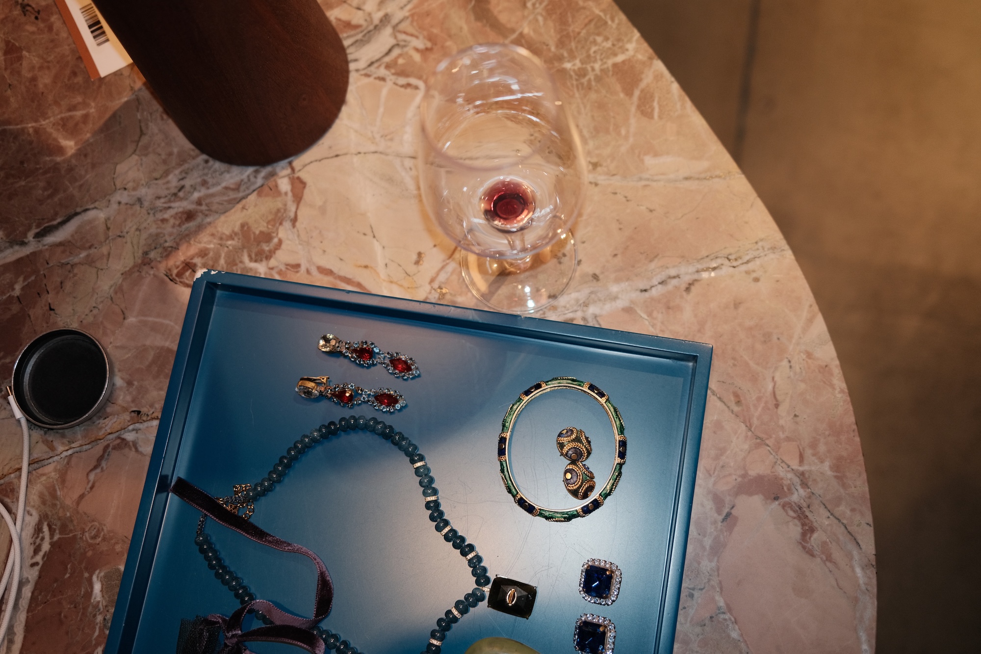 Vintage costume jewellery on a blue tray next to a glass of red wine on a marble table
