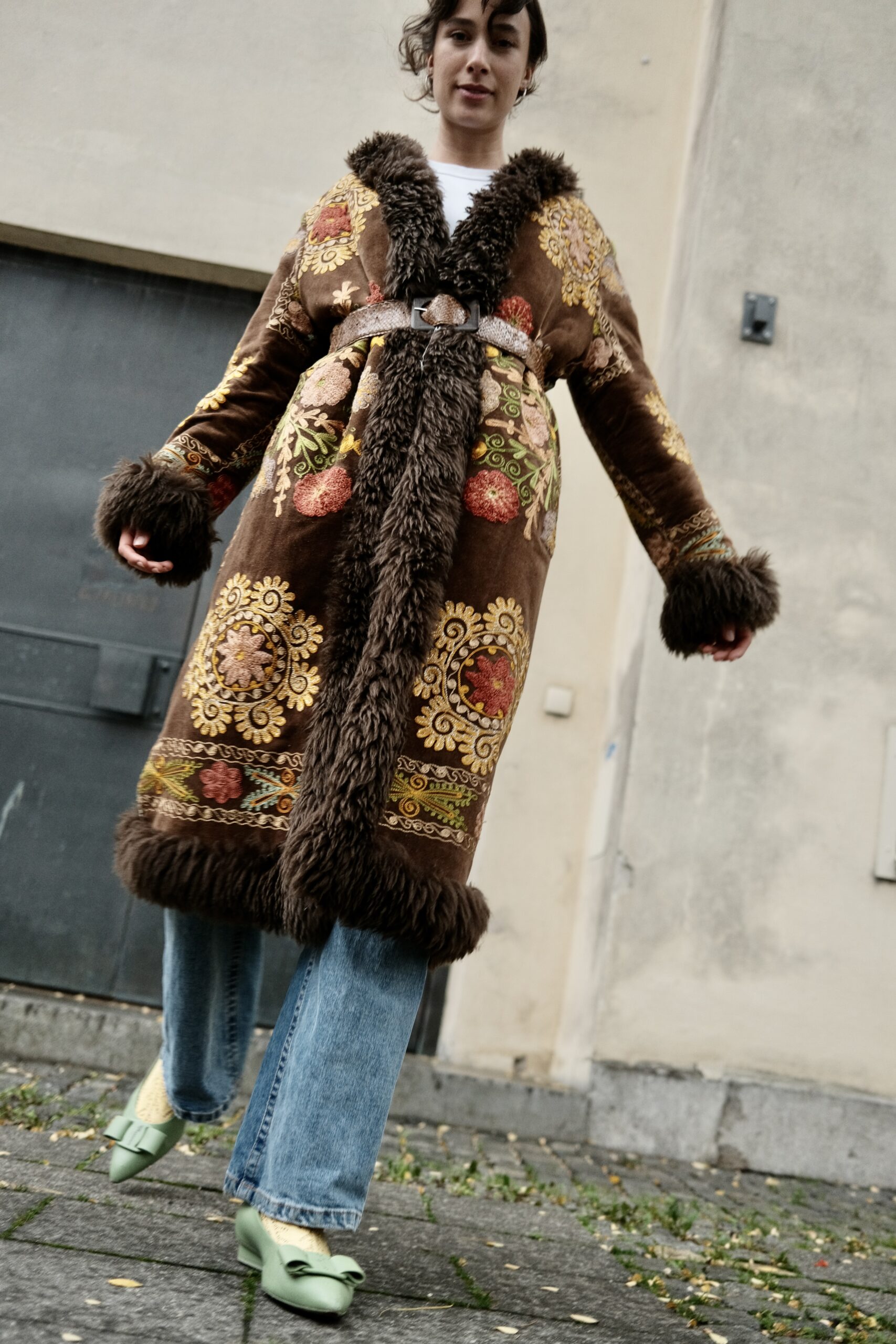 A woman in an embroidered vintage velvet coat with shaggy trim and wide jeans